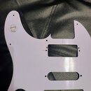 Bílá plastová pickguard pro elektrickou kytaru. V levé horní části je viditelný kulatý štítek s nápisem genuine Fender®. Povrch vykazuje drobné škráb…