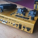 Zlatý kytarový procesor BOSS GP-10 s dvěma černými pedály a jedním černým přepínačem. Na přední straně je nápis BOSS GP-10 GUITAR PROCESSOR a na zadn…