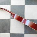 Fotografie zachycuje bok kytary v červenobílé barvě s tmavě hnědým dřevěným povrchem. Podél hrany těla je vidět ozdobný bílo-žlutý pruh. Na hlavě nás…