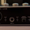Černý zvukový interface s kovovým stříbrným rámem. Na přední straně jsou nápisy U-PHORIA UM2 a logo behringer, vstup MIC/LINE 1 s nápisem XENYX MIC P…