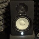 Černý studiový monitor v hranatém korpusu s matným povrchem. Má dvě jednotky: horní malý výšek s mřížkou a spodní větší basový reproduktor se světlou…