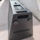 Černý trapezoidní reproduktor s texturovaným povrchem. Na horní a boční straně jsou vidět montážní otvory s imbusovými šrouby a úzké ventilační mřížk…