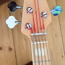 Hlava a hриф basové kytary z přírodního dřeva s červenými strunami. Na hlavě je nápis Marcus Miller a logo ve tvaru stylizovaného písmena S. Nástroj…