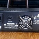 Zadní strana černého basového zesilovače značky aguilar. Jsou zde dva výstupy SPEAKER OUTPUTS s nápisem 4 OHM MINIMUM TOTAL LOAD, výstup TUNER OUTPUT…