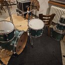Sada bubnů v tmavě zeleném provedení. Na blanách jsou viditelné nápisy EVANS a REMO. Soubor obsahuje basový buben, dva tom-tomy a jeden floor tom. Ná…