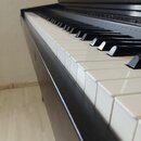 Detailní pohled na klávesnici černého pianina. Jsou vidět bílé a černé klávesy v dobrém stavu. Na černém lakovaném povrchu korpusu jsou viditelné dro…