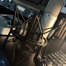 Černý pavoukový držák z plastu s viditelnou texturou 3D tisku. V pozadí je stříbrný kondenzátorový mikrofon s kovovou síťkou. Na fotce nejsou žádné č…
