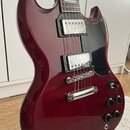 Tmavě červená elektrická kytara s černým plechtrátem. Na obou snímačích je viditelný nápis "Epiphone". Kytara má chromovaný most a stopku, čtyři ovlá…