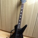 Černá elektrická kytara s asymetrickým tělem typu Explorer umístěná na stojanu. Na hlavě hmatníku je bílý nápis GT Epiphone. Hmatník je tmavého dřeva…
