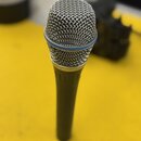 Dynamický mikrofon s kovovou síťovkou stříbrné barvy a tmavě šedým tělem. Mezi síťovkou a tělem je vidět tenký modrý prstenec. Na přístroji nejsou žá…