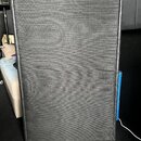 Černý basový reproduktor v hranatém kufru potaženém černým vinylen. Přední strana je zakrytá černou textilní ochrannou síťkou, za kterou jsou vidět o…