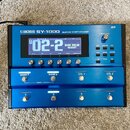 Modrý kytarový syntetizátor s nápisem BOSS SY-1000 GUITAR SYNTHESIZER. Zařízení má digitální displej, na kterém je zobrazen text 02-2 a WARM DREAD NO…