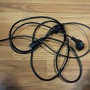 Na fotografii je černý elektrický napájecí kabel sviditelným síťovým konektorem a dvěma dalšími koncovými konektory. Kabel je složen do několika smyč…