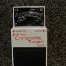 Bílý kytarový ladič s černým spínacím pedálem. Na spodní části je červený nápis Chromatic Tuner TU-3 a šipky OUTPUT, BYPASS a INPUT. Horní část obsah…