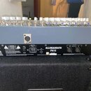 Šedý mixovací pult s bílými ovratovými knoflíky. Na zadním panelu je nápis ALLEN&HEATH PA12, označení MAIN INPUT a MAIN OUTPUT s konektory A a B. Jso…