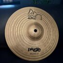 Kruhový mosazný činel s koncentrickým žebrováním povrchu. Na horní části je logo Paiste a nápis ALPHA, ve spodní části je nápis PAiste a pod ním SPLA…