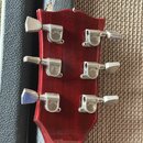 Zadní strana červené kytarové hlavy s šesti chromovanými ladičkami. Na každém z ladiček je vyryto logo GIBSON. Povrch lakovaného dřeva vykazuje drobn…