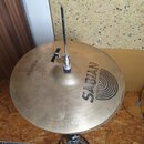 Kruhové mosazný činely umístěné na stojanu. Na povrchu je černý nápis „SABIAN“ a doprovodný grafický prvek ve tvaru koncentrických oblouků. V horní č…