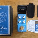 Modře lakovaný efekt pedál s nápisy Blue Rain, Overdrive a True Bypass. Na pedálu jsou tři bílé ovládací knoflíky s popisky VOLUME, TONE a HIGH. Souč…