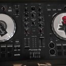 Černý DJ 컨트롤러 Pioneer Dj s logem serato v dolní části. Zařízení má dva stříbrné jog-wheels, z nichž oba jsou zakryty nálepkami; na levém je nápis The…
