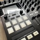 Detailní pohled na černý DJ kontrolér s kovovým povrchem. Na zařízení jsou vidět bílé podsvícené pady s nápisy HOTCUE, FREEZE, REMIX a FLUX, dále tla…