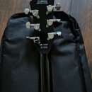 Černá hlava kytary s nápisy CYJ2502203 a CRAFTED IN CHINA v horní části. Ve spodní části je uveden model LM-1987 a symboly CE. Na ladičkách jsou vidi…
