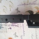 Černý plastový přístroj s několika konektory a ovládacími prvky. Na spodní hraně jsou viditelné nápisy DC 5V, USB, OUTPUT a AUX IN. U konektoru pro v…