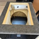 Fotografie zachycuje otevřenou dřevěnou bednu, pravděpodobně basový reproduktor nebo subwoofer. Povrch je potažen šedým plstěným materiálem, vnitřní…