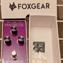 Fialový kytarový efekt s bílým rámem a nápisem MAITRESSE. Na spodní části je logo FOXGEAR, v horní části jsou nápisy OUTPUT, POWER a INPUT. Efekt má…