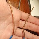 Na dlani je drženo dvě krátká elektrická kabelážní spoje s opleteným kovovým povrchem v měděné barvě. Konce kabelů jsou zakončeny modrými krytkami. V…