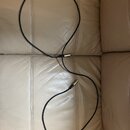 Černý instrumentální kabel s kovovými konektory. Kabel je položen na béžovém koženém povrchu. Na kabelu ani konektorech nejsou viditelné žádné značky…