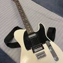 Bílá elektrická kytara typu Telecaster s černým pickguardem a černým popruhem. Na hlavě hmatníku je viditelné logo Fender. Nástroj má dva snímače s k…