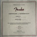 Fotografie znázorňuje papírový certifikát pravosti s nápisy v černé a červené barvě. V horní části je text GENUINE PRODUCT OF FENDER a červené logo F…