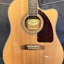 Akustická kytara s cutawayem, světlým dřevěným povrchem a tmavě hnědým pickguardem. Uvnitř otvoru rezonátoru je štítek s nápisy GUARANTEED, Epiphone…