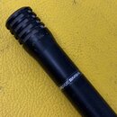 Černý dynamický mikrofon s žebrovanou hlavicí. Na těle je bílý nápis SHURE SM94. Povrch vykazuje známky opotřebení v podobě oděraného laku a drobných…