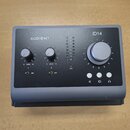 Šedý audio rozhraní s matným povrchem. Na předním panelu je velký ovládací knoflík, dva menší knoflíky s nápisy GAIN 0 10 a přepínače 48V. Jsou zde v…