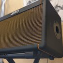 Černý kytarový kombo zesilovač s hnědou mřížkou reproduktoru. Na horní hraně je bílý nápis JOYO. Povrch je potažen černým vinylen s oranžovými lemový…