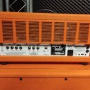 Zadní strana oranžového kytarového zesilovače s kovovým chassis. Na zadním panelu jsou viditelné nápisy ORANGE, RK50H MK II a LONDON ENGLAND. Jsou zd…
