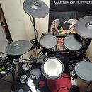 Elektronická bicí souprava s černými pady a činely na černém kovovém rámu. Na modulu je vidět nápis YAMAHA a označení DTX. Na jednom z padů je bílý n…