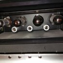 Fotografie zachycuje vnitřek přístroje s четыma elektronkami uspořádanými v řadě. Pod každou elektronkou se nachází kovový soket. Zařízení má černý p…