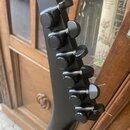Detail hlavy černé elektrické kytary s šesti ladicími kolíky. Nástroj má matný černý povrch a černé kovové hardware. Na viditelné části hlavy nejsou…