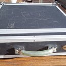Černý transportní kufr s hliníkovými hranami a kovovými rohy. Na přední straně je plastová rukojeť a oválný štítek s nápisem ROCKCASE. Povrch víka vy…