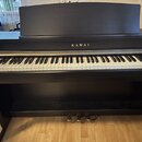 Černý digitální piano s klaviatura a integrovaným stojanem. Na přední straně nad klávesami je zlatý nápis KAWAI. Nástroj má v horní části připevněný…