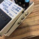 Bílý efekt pedál s modrými ovratovými knoflíky. Na horní části je nápis Digital Delay DD-7 a označení vstupů a výstupů OUTPUT B, OUTPUT A (MONO), INP…