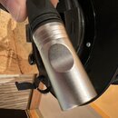 Detailní pohled na spodní část stříbrného mikrofonu z kovu. Na povrchu je vyražen nečitelný nápis v kruhovém poli. Horní část mikrofonu je černé barv…
