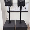 Dva černé aktivní reproduktory umístěné na stojanů nad dvěma černými subwoofery. Na zadních panelech reproduktorů jsou viditelná loga YAMAHA a označe…