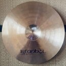 Kruhový činel z mosazného kovu s viditelným broušením povrchu. V dolní části je nápis „istanbul Agop Made in Turkey“. Na centrálním kopulku je nalepe…