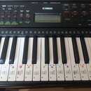 Černý digitální klavír značky YAMAHA. Na displeji je viditelný nápis GrandPno a čas 10:01. Na bílých klávesách jsou nalepené papírové štítky s označe…