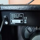 Detail zadní strany černého komba s povrchem z imitace kůže. Na černém štítku je bílý text: „POWER SOURCE: 230 V ~ 50/60Hz“, „POWER CONSUMPTION: 15W…