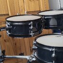 Sada černých bubnů na chromovaném stojanu. Na blanách jsou viditelná loga značky Mapex. Povrch nástrojů je glossy černý, s chromovaným kováním.